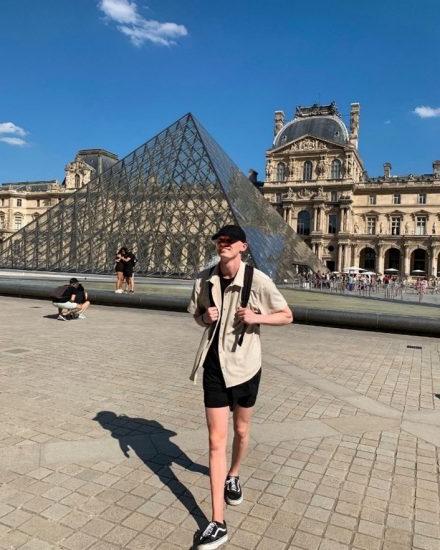 A young male in front of a glass pyramid in France.