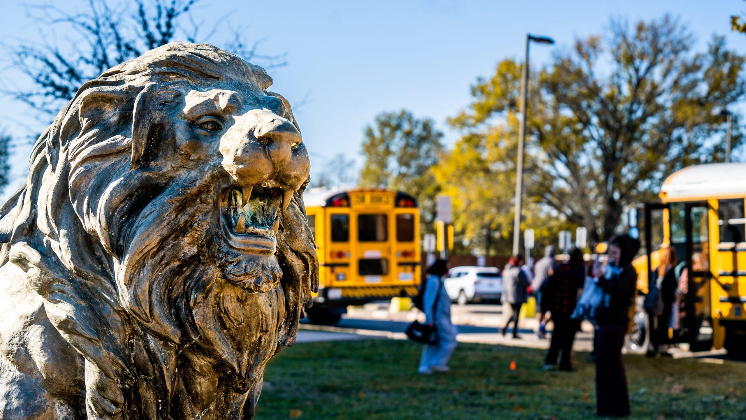 The lion statue with buses in the back ground. 